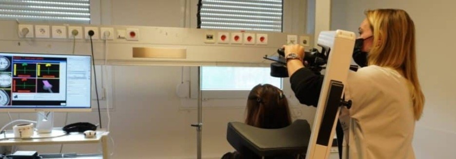 Une personne manipule le bras d'une machine de stimulation magnétique transcranienne pour délivrer le traitement à une personne allongée de dos dans un fauteuil