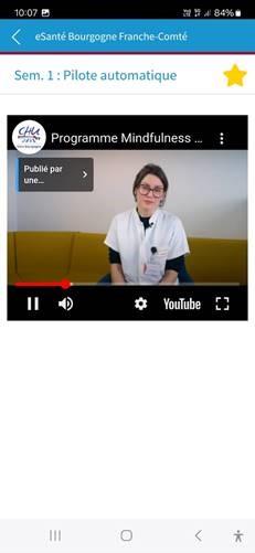 Capture d'écran de l'application smartphone eMind sur laquelle on voit un menu indiquant un retour au menu principal, l'intitulé de la page "Sem. 1 : Pilote automatique" et une vidéo montrant une médecin assise